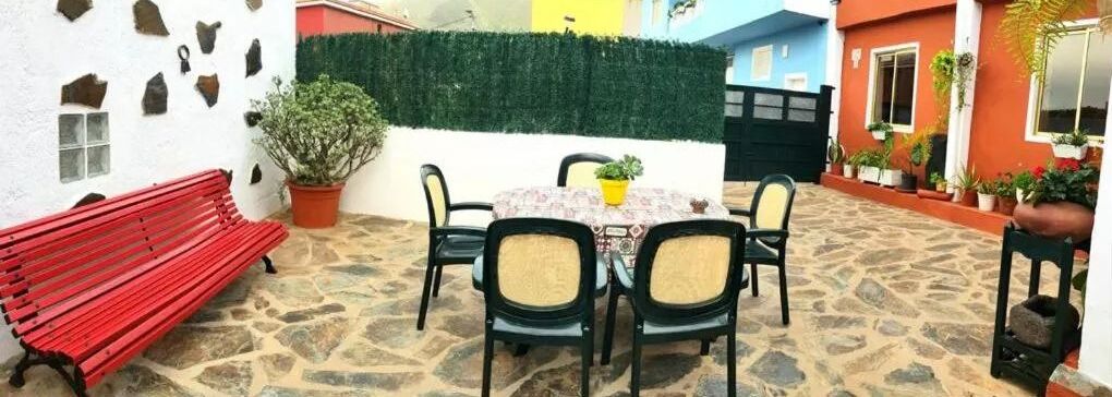 A patio with a round table, four chairs, a red bench, and potted plants.