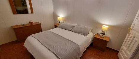 A bedroom with a bed, two bedside tables, a dresser, a mirror, and two wall-mounted lights.