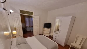 Ein Schlafzimmer mit Bett, Fernseher auf einem Schrank, Kleiderschrank und Schreibtisch mit Stuhl.