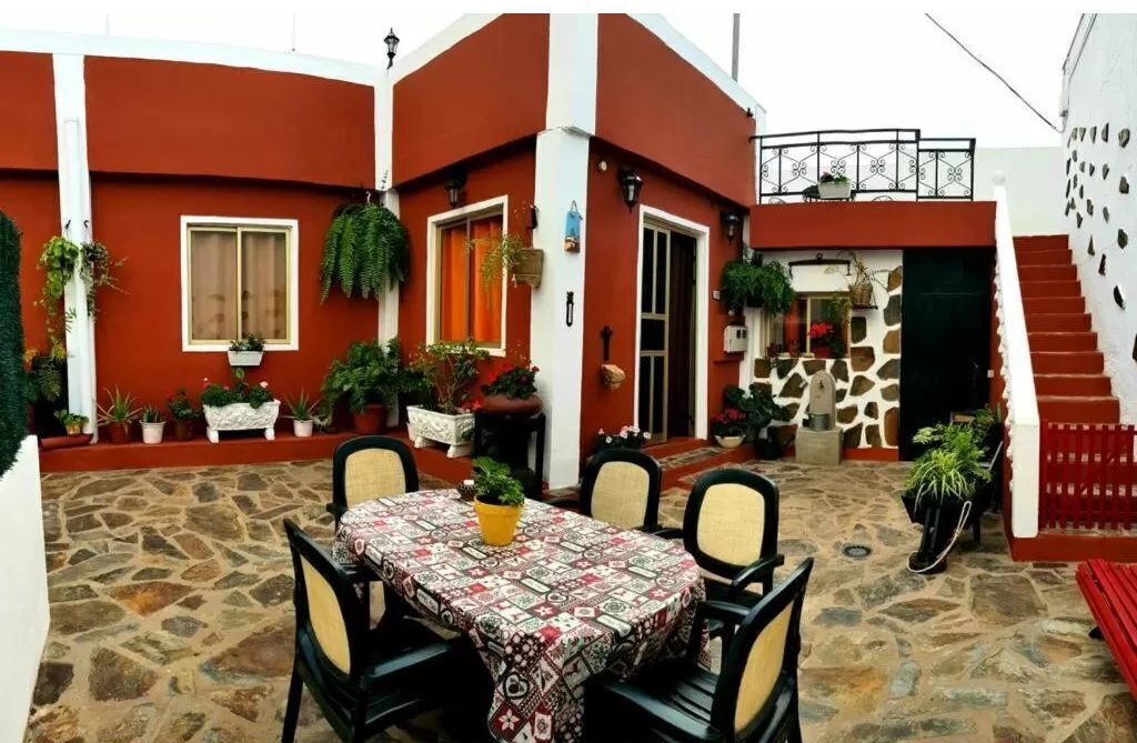 A patio area with a table and chairs, surrounded by potted plants and a stone floor.