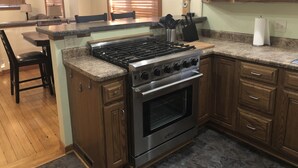 Een keuken met een centraal eiland, houten kastjes, een roestvrijstalen kookplaat en een inbouwoven.