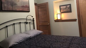 Een slaapkamer met een bed, een houten deur, een lijst met een foto en een wandlamp.