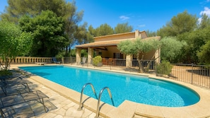 A swimming pool with a stone deck, surrounded by a fence, and a building with a tiled roof in the background. - Le Domaine d'Alèzen (Grans)