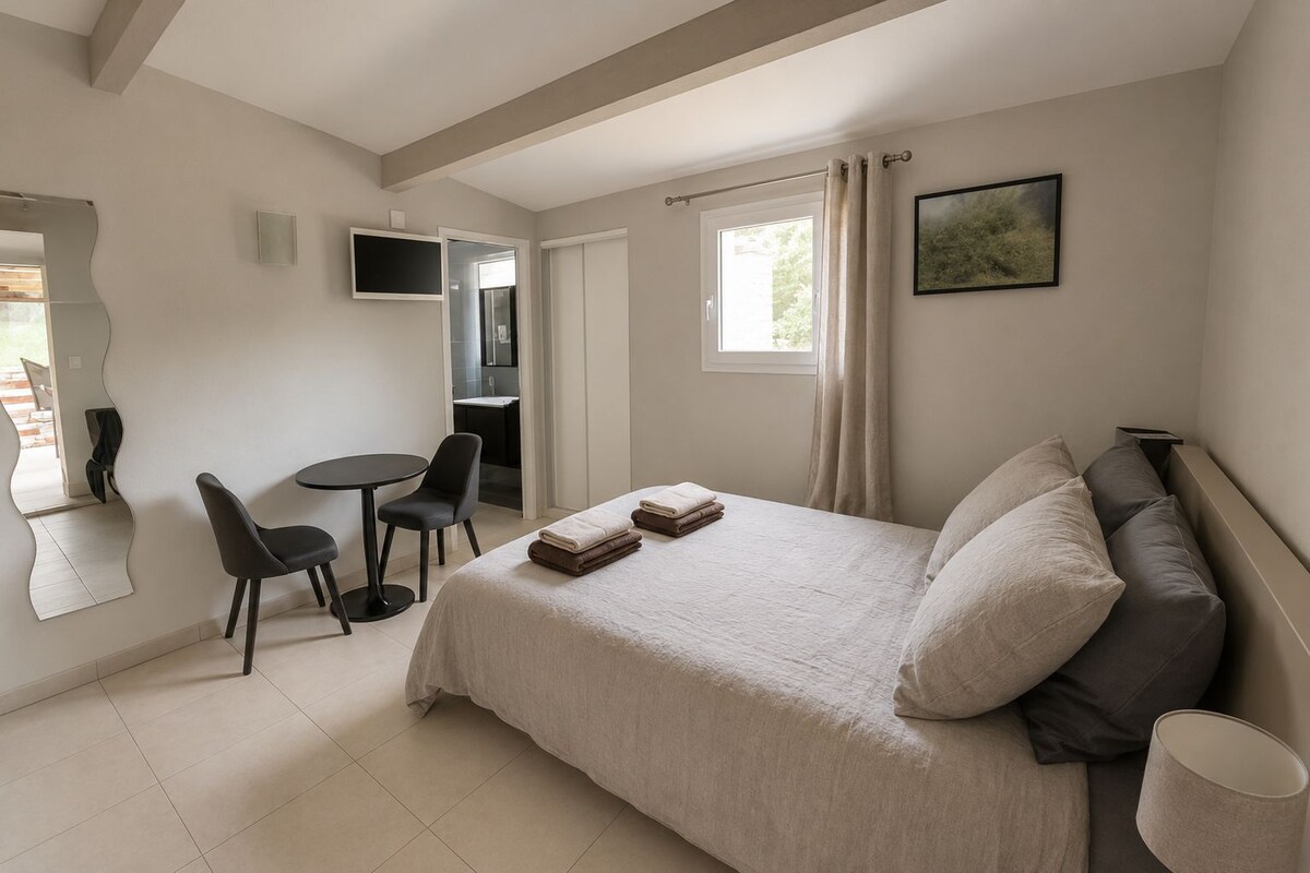 A bedroom with a bed, a desk, chairs, a TV, and a window.