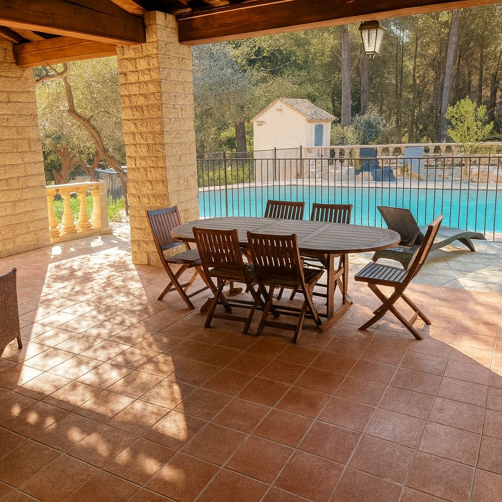 A covered outdoor area with a pool, a table with chairs, and a stone wall.