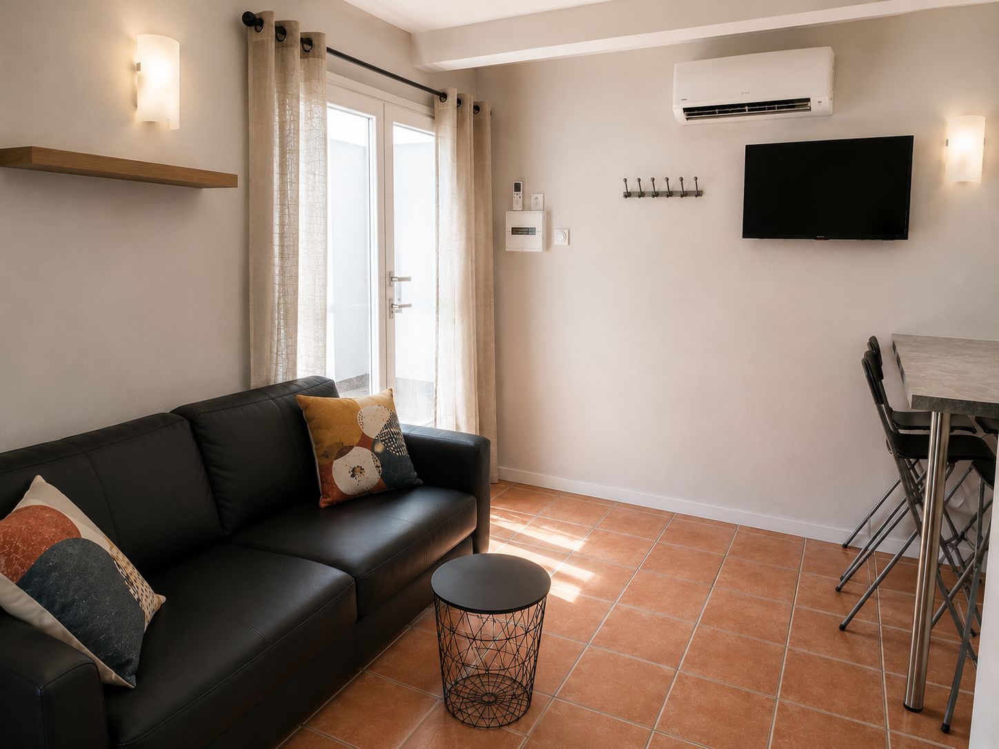 A modern living room with a black leather sofa, a round coffee table, and a dining area with a metal chair and table.