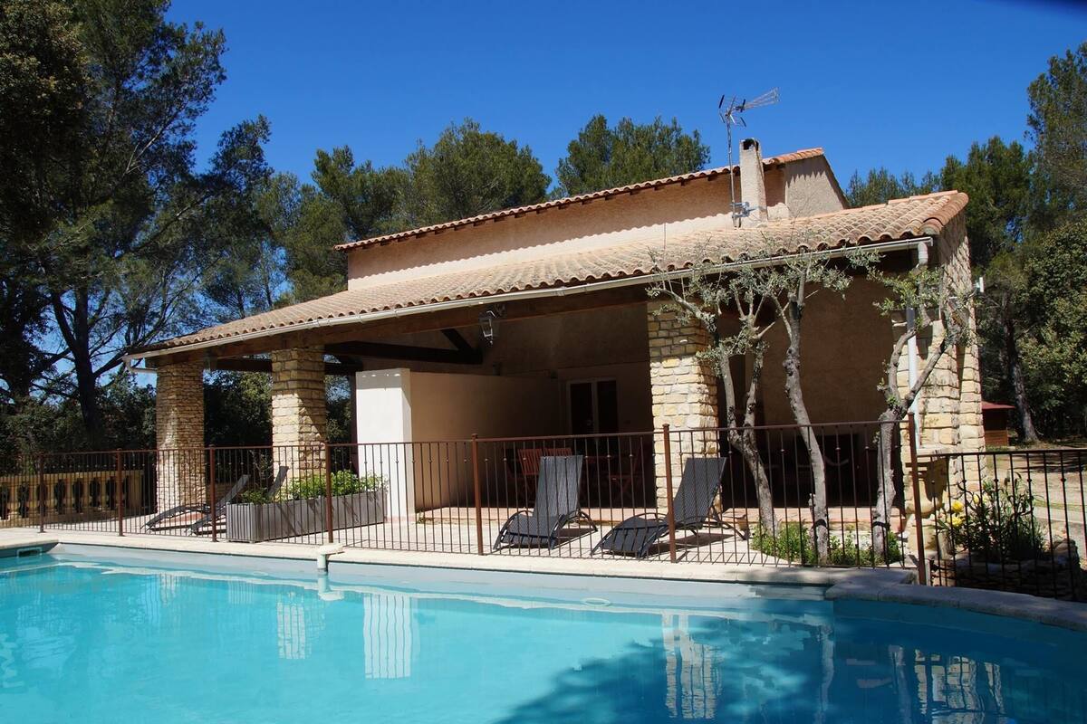 A poolside villa with a covered patio, stone pillars, and a clear blue pool.
