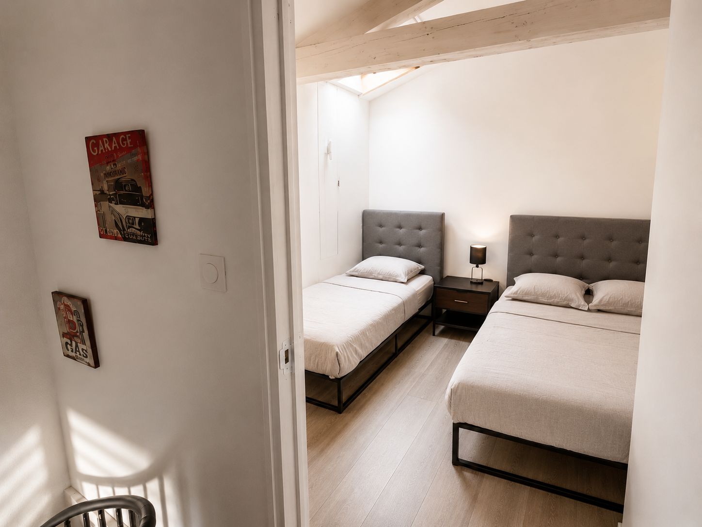 A bedroom with two beds, a nightstand, and a wall-mounted light.