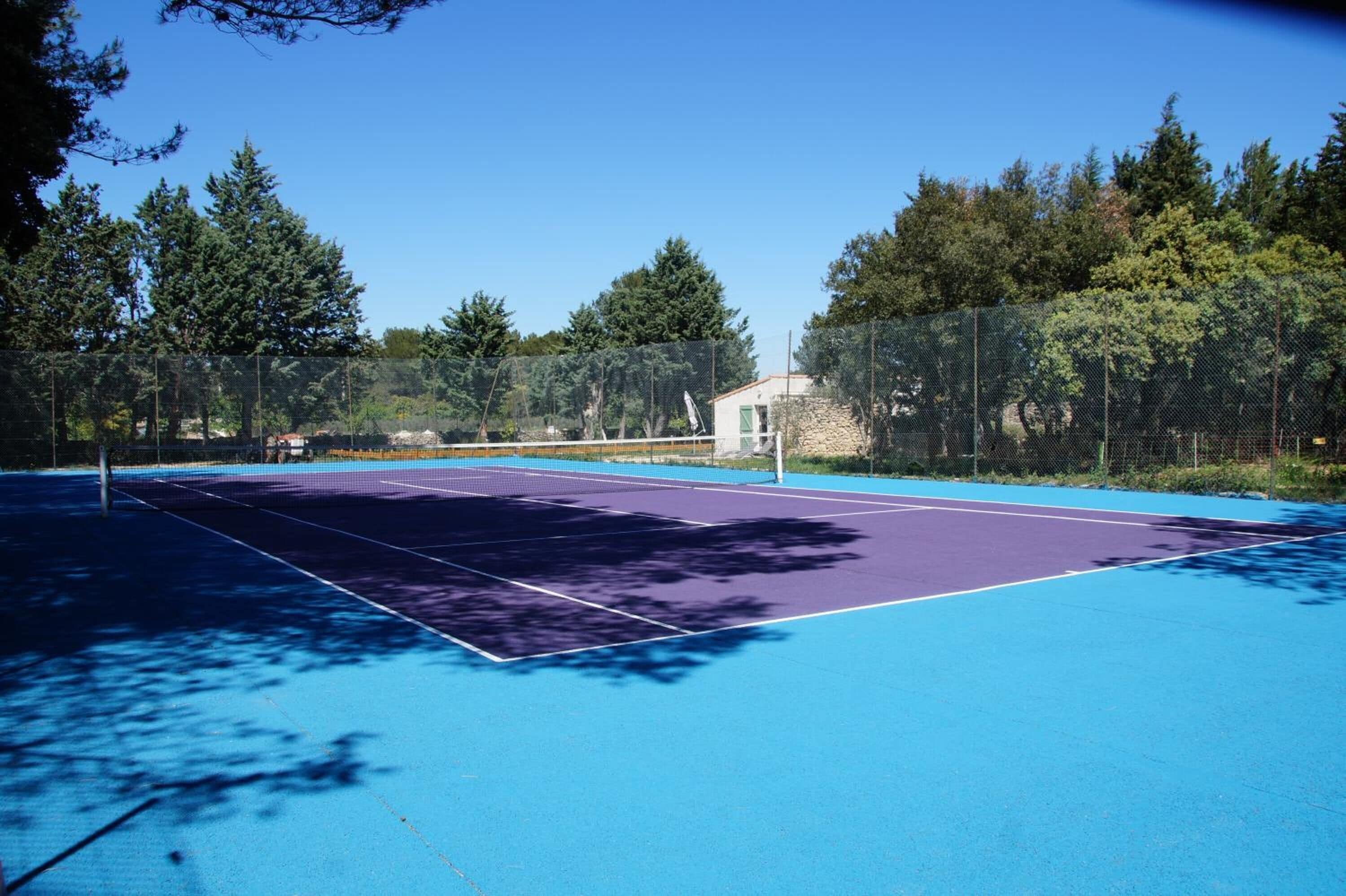 An outdoor tennis court with a net, surrounded by trees and a fence.