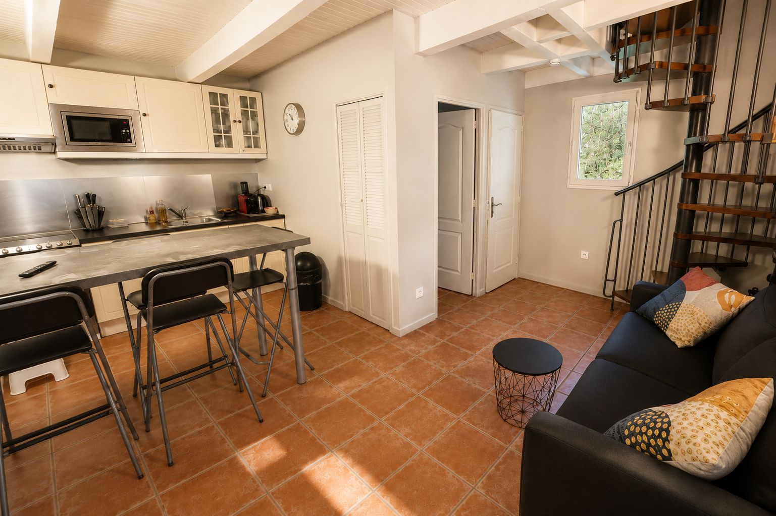 A compact kitchen with a microwave, cabinets, and a dining area with stools.