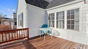 A wooden deck with a table and chairs, a white exterior wall, and a window with curtains. - Charming 1940's Cottage in central location (Rapid City)