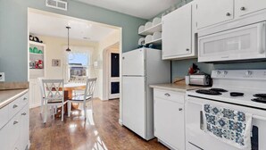 A kitchen with white cabinets, a stove, a microwave, and a dining area with a table and chairs. - Charming 1940's Cottage in central location (Rapid City)