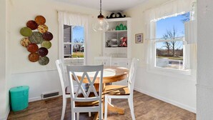 A dining area with a round table, white chairs, a hanging light fixture, and a window with a view. - Charming 1940's Cottage in central location (Rapid City)