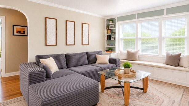 A living room with a sectional sofa, a glass coffee table, a bookshelf, and a window with blinds. - Charming 1940's Cottage in central location (Rapid City)