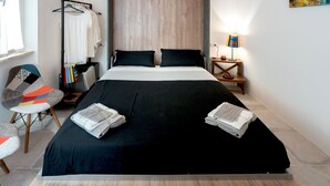 Una habitación de hotel moderna con una cama grande, una silla, una mesita de noche y un televisor montado en la pared.