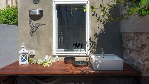 Un pequeño espacio de cocina al aire libre con un lavamanos blanco, una mesa de madera y un farol decorativo.