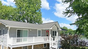 A two-story house with a stone foundation, a front porch with white railings, and a red door.