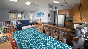 A spacious living area with a dining table, a sofa, and a kitchen with wooden cabinets and a refrigerator.
