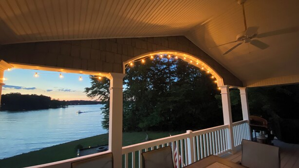A covered outdoor area with a view of a lake, string lights, and a ceiling fan.