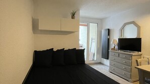 Une petite chambre comprenant un lit, un bureau, une télévision et une petite plante.