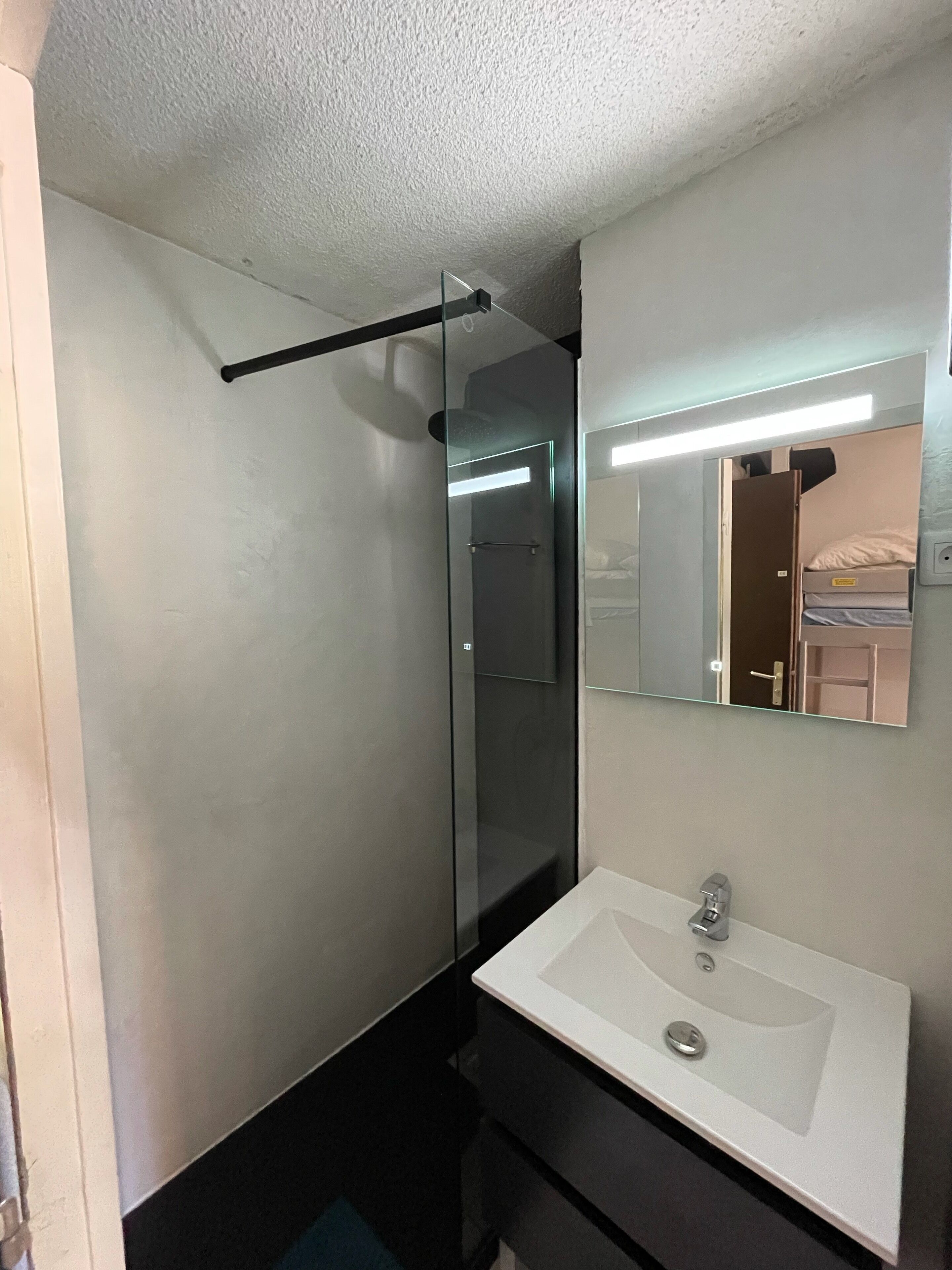 A bathroom with a white sink, a glass shower enclosure, and a mirror above the sink.