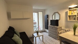 Un salon moderne avec un canapé noir, une petite table ornée d’une plante et un coin repas comprenant une table et des chaises.