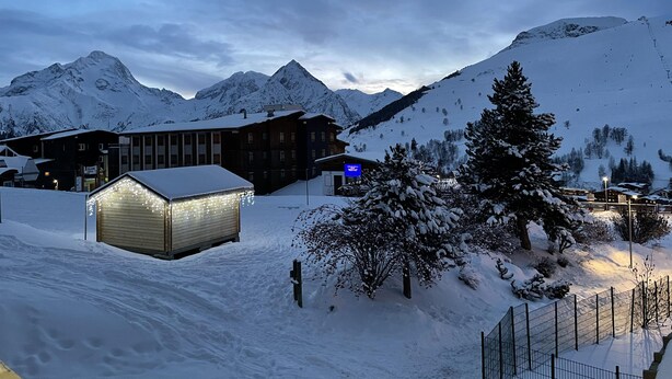 Un paysage montagneux enneigé, avec un bâtiment doté de nombreuses fenêtres et d’une enseigne illuminée.