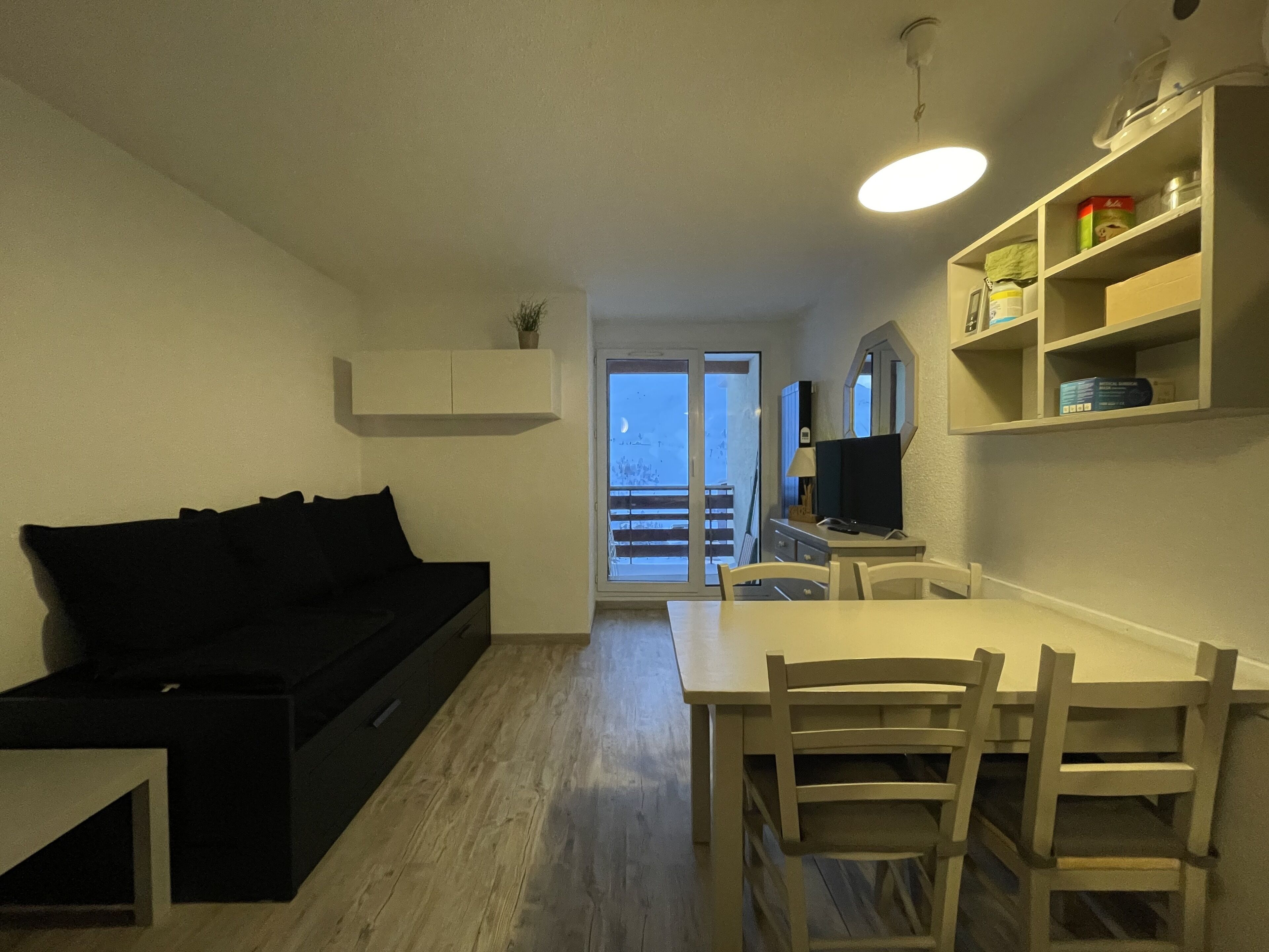 Un espacio habitable compacto con sofá, una mesa de comedor con sillas, televisor y balcón con vistas.