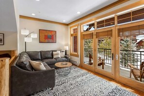 A modern living room with a leather sofa, a patterned rug, and a large window with a view of the outdoors.