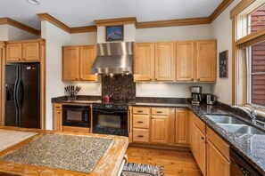 A kitchen with wooden cabinets, a stainless steel range hood, granite countertops, a refrigerator, an oven, and a sink.