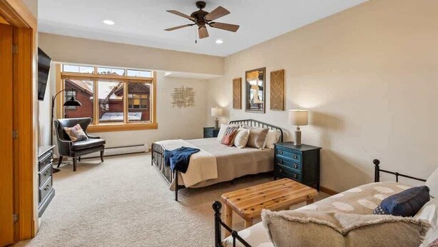 A bedroom with two beds, a desk, a chair, a ceiling fan, and a window with a view of a building. - Lodge-style Condo in the Heart of Big Sky (Big Sky)