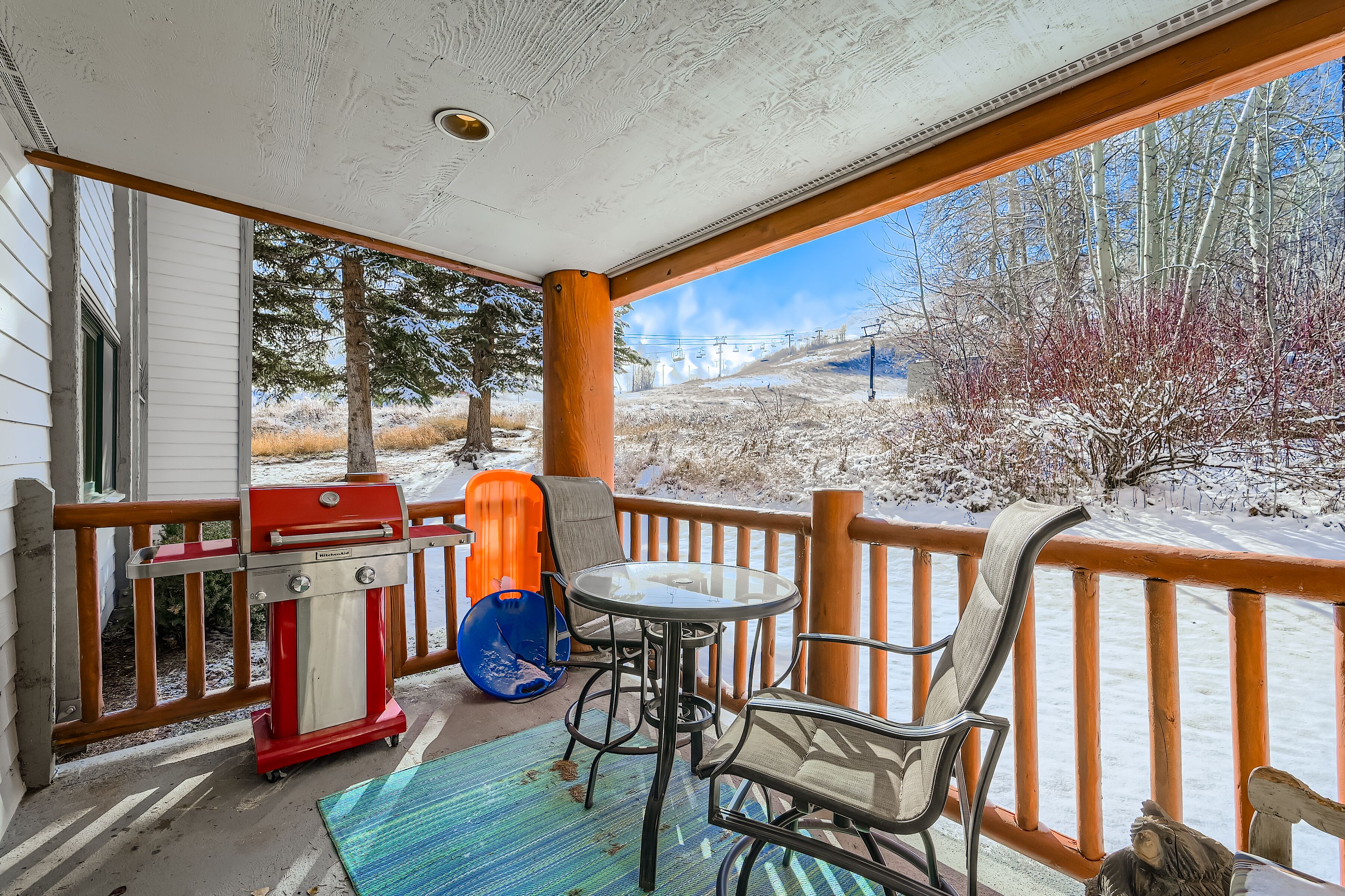 A covered porch with a grill, chairs, and a view of a snowy landscape.