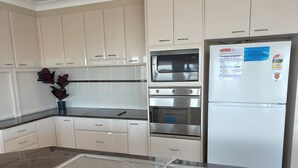Eine moderne Küche mit weißen Schränken, einer Edelstahl-Spüle, einem eingebauten Backofen und einem Kühlschrank.