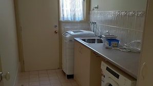 Eine kleine Küche mit Waschmaschine, Spüle und einem Fenster mit Vorhängen.