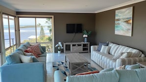 Ein Wohnzimmer mit großem Fenster, einem an der Wand befestigten Fernseher und einem Gemälde über der Couch.