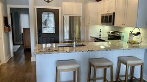 A kitchen with white cabinets, a stainless steel refrigerator, a microwave, and a sink. There are three wooden stools at the island. - Breathtaking lake views, steps from beach, golf, and clubhouse. Renovated home! (Big Canoe)