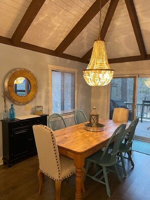 Un coin repas avec une table en bois, quatre chaises, un lustre et une grande fenêtre.