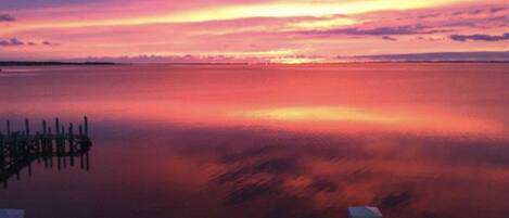 Un coucher de soleil sur une étendue d’eau calme, avec une jetée en bois au premier plan.