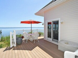 Eine Holzterrasse mit Tisch und Stühlen, einem roten Sonnenschirm und Blick auf das Wasser.