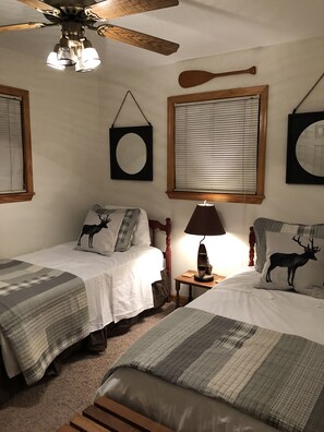Een slaapkamer met twee bedden, een plafondventilator, een lamp en een houten peddel aan de muur.