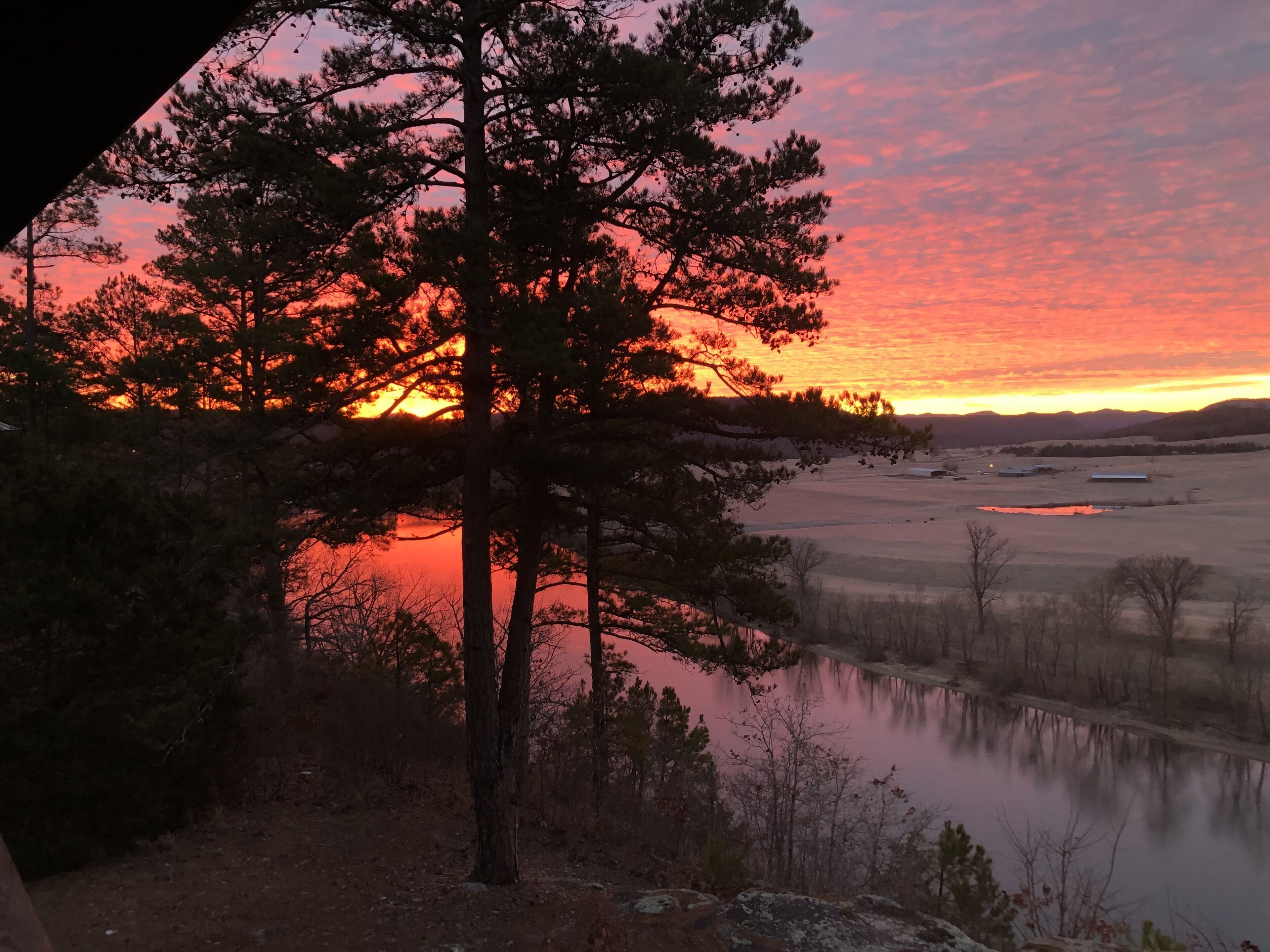 A sunset over a lake with trees in the foreground.