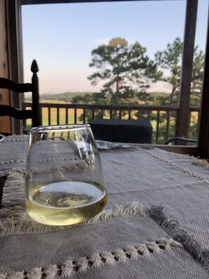 Een glas witte wijn op een geribbelde tafelkleed, met uitzicht op een houten terras en bomen op de achtergrond.