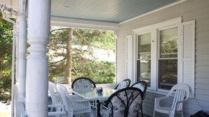 A covered porch with a table and chairs, a window with shutters, and a tree in the background. - Spacious Updated Victorian, A/C, Walk to Beach, Close to Town  (Narragansett)