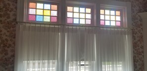 A room with a window featuring colorful stained glass panes and sheer white curtains. - Spacious Updated Victorian, A/C, Walk to Beach, Close to Town  (Narragansett)
