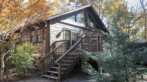 Un rustico chalet con una scala in legno che conduce a un balcone, circondato da foglie autunnali.