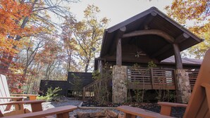 Un chalet avec des fondations en pierre, une terrasse en bois et un espace extérieur couvert doté d’un ventilateur de plafond.