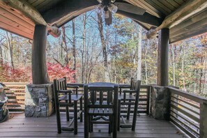 A covered outdoor area with a wooden table and chairs, surrounded by stone pillars and a wooden railing. - Treehouse B - A Suite Getaway for Two (Bryson City)