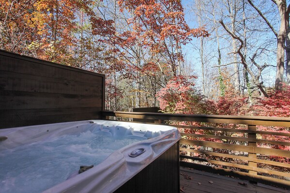 Un bain à remous sur une terrasse en bois, avec vue sur les arbres aux couleurs automnales.