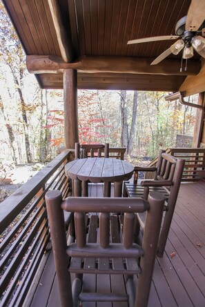 A wooden deck with a round table and chairs, surrounded by a wooden railing, overlooking a forested area. - Treehouse B - A Suite Getaway for Two (Bryson City)