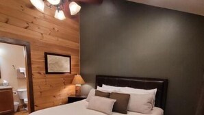 Une chambre avec un grand lit, des murs en bois, un ventilateur de plafond et un tableau encadré accroché au mur.